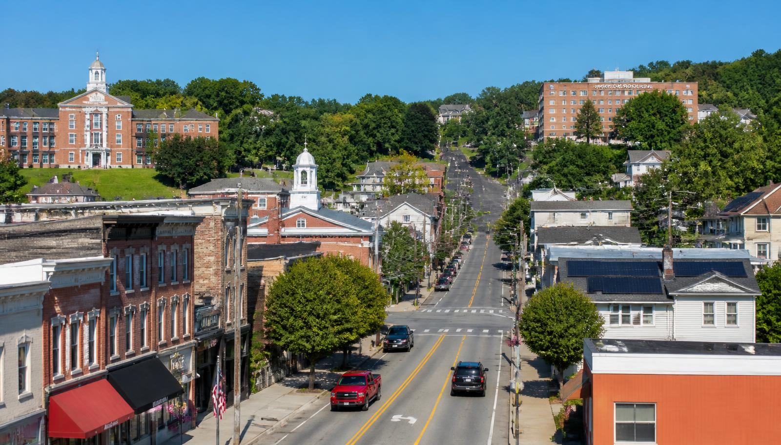 A small town main street in bright daylight with civic buildings, homes, trees, and rooftop solar