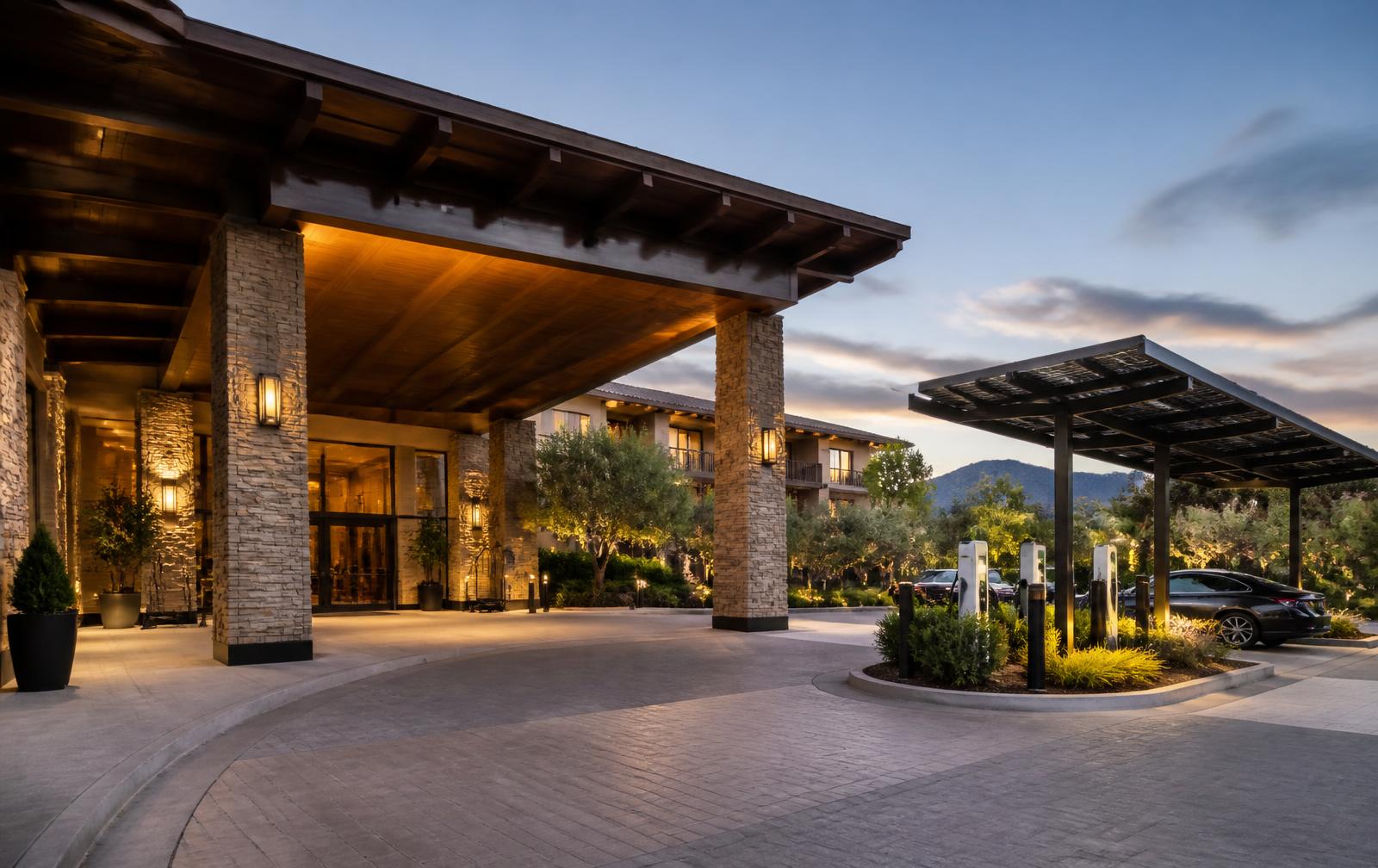 Upscale hotel arrival court at dusk with an adjacent solar canopy and integrated guest charging stations